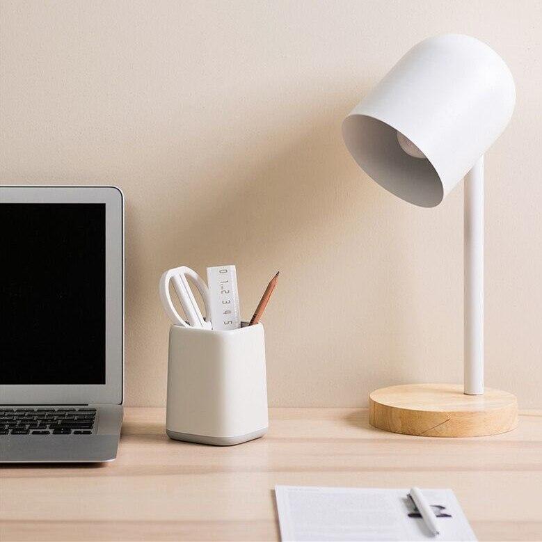white and gray pen holder on table next to macbook and lamp