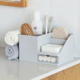 gray desktop organizer on bathroom counter holding hand towels, tooth brushes, and toiletries